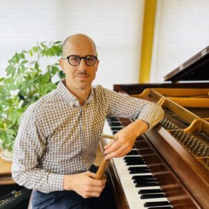 Justin Klein posing at his piano holding a tuning lever